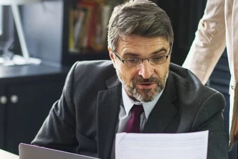 Homme en costume lisant un document, lunettes sur le nez, un collègue à ses côtés