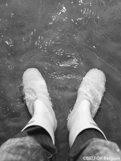 Pieds chaussés de bottes en caoutchouc dans une pièce inondée, photo en noir et blanc