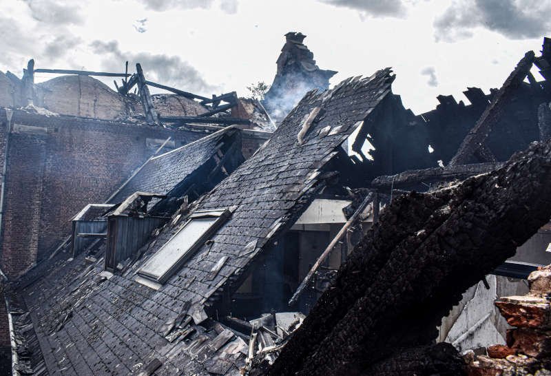 Toiture d'une maison effondrée et calcinée après un incendie, fumée encore visible