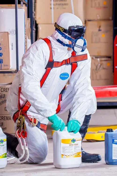 Technicien en combinaison de protection et masque respiratoire préparant des bidons de produit de décontamination