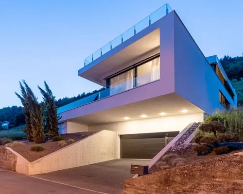 Maison contemporaine à toit plat et grandes baies vitrées, éclairée au crépuscule