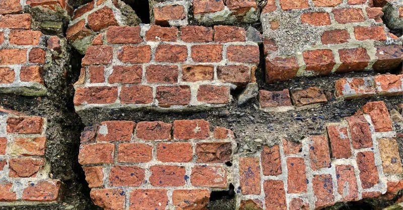 Mur de briques profondément fissuré, maçonnerie disjointe par un mouvement du sol