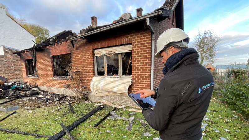 Expert en veste Expertises EAB prenant des relevés sur tablette devant une maison incendiée