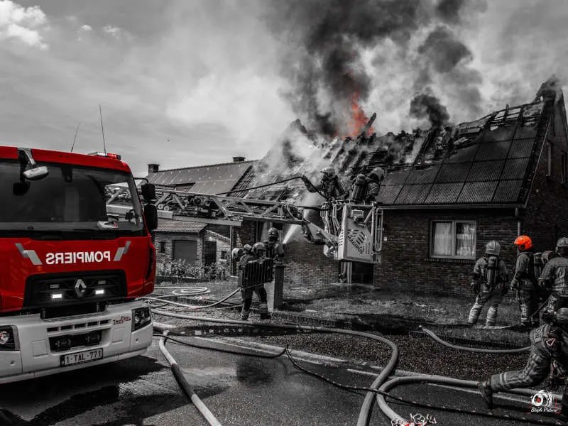 Pompiers luttant contre l'incendie d'une toiture de maison, camion de pompiers et tuyaux au premier plan