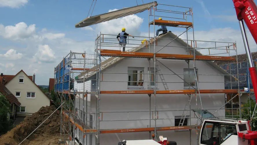 Maison en reconstruction entourée d'échafaudages, grue posant un élément de toiture